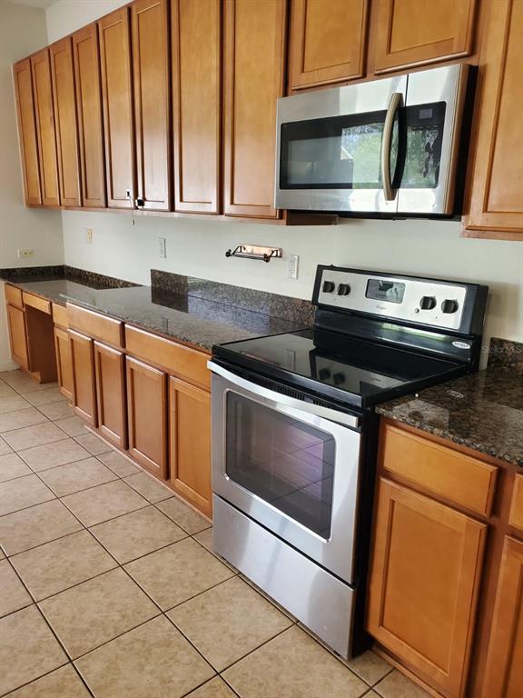 A kitchen features wood cabinets, granite countertops, stainless steel appliances, and beige tile flooring — 12148 LUFTBURROW LANE, HUDSON, FL
