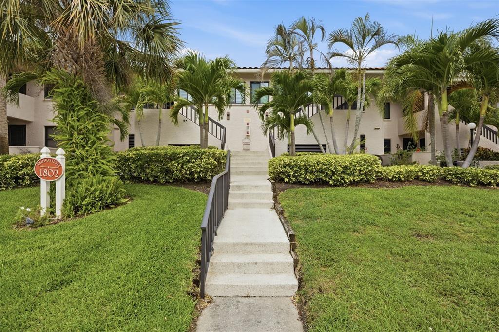 A two-story apartment building with a red tile roof, palm trees, and a concrete walkway — 1802 MARINER DRIVE E UNIT 25, TARPON SPRINGS, FL