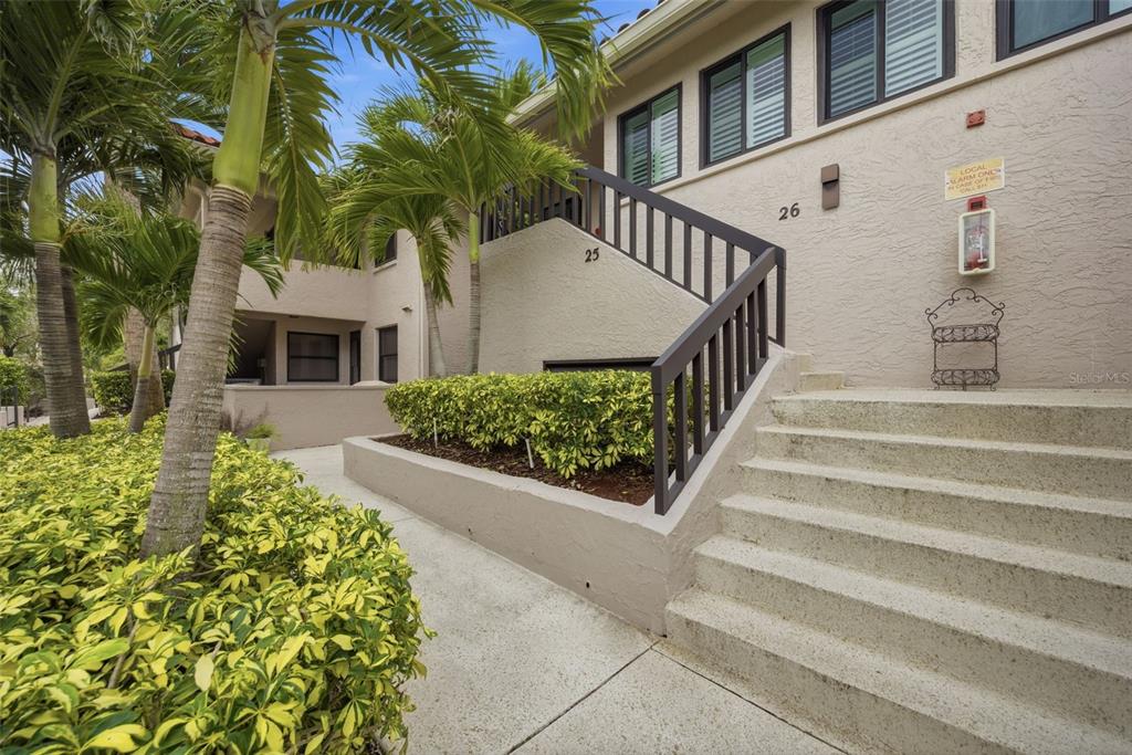 Exterior view of a multi-story building with concrete stairs, a wooden railing, and palm trees — 1802 MARINER DRIVE E UNIT 25, TARPON SPRINGS, FL