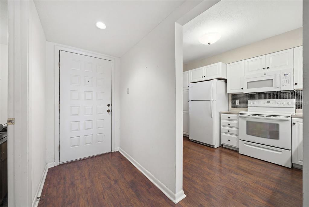 A kitchen features white cabinets, white appliances, a tiled backsplash, and wood-look flooring — 1802 MARINER DRIVE E UNIT 25, TARPON SPRINGS, FL