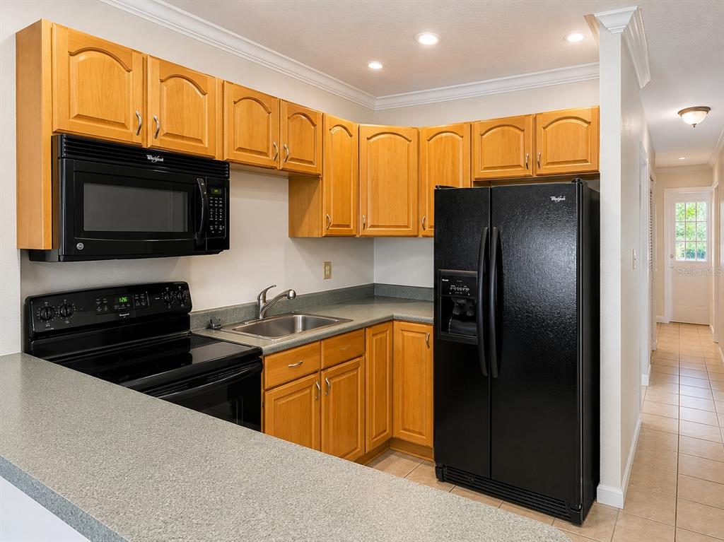 A kitchen features light wood cabinets, black appliances, and gray countertops — 2500 HARN BOULEVARD UNIT F24, CLEARWATER, FL
