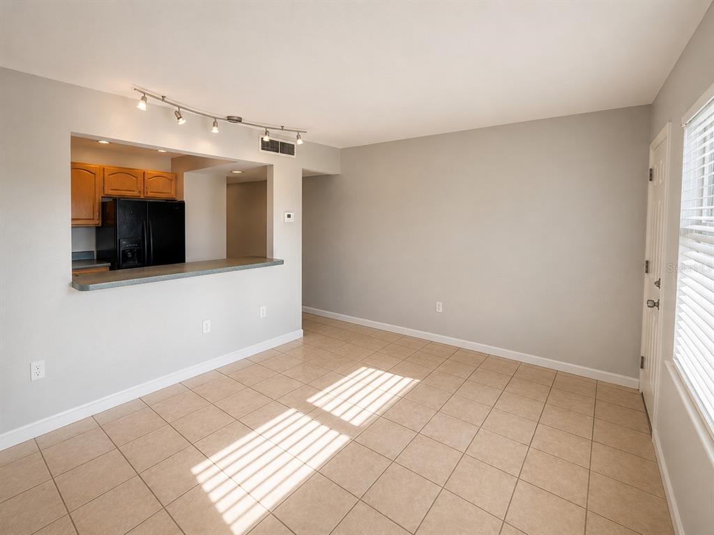 An empty room with beige tile flooring, light gray walls, and a kitchen pass-through window — 2500 HARN BOULEVARD UNIT F24, CLEARWATER, FL