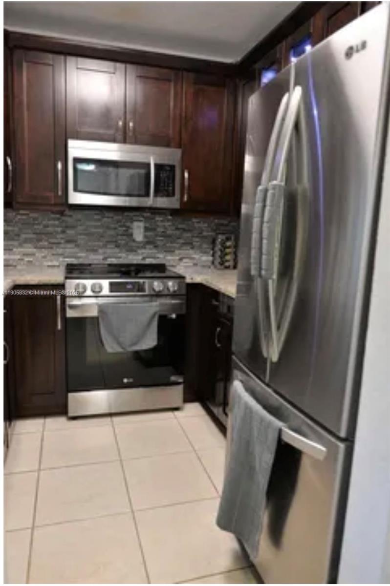 A kitchen features dark wood cabinets, stainless steel appliances, a tiled backsplash, and light flooring — 10900 SW 104th St # 314, Miami FL 33176, MIAMI, FL