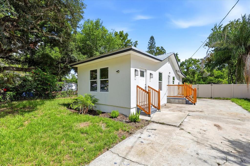 A small white house with a metal roof and wooden porch railings sits on concrete — 7206 RHODE ISLAND DRIVE, TAMPA, FL
