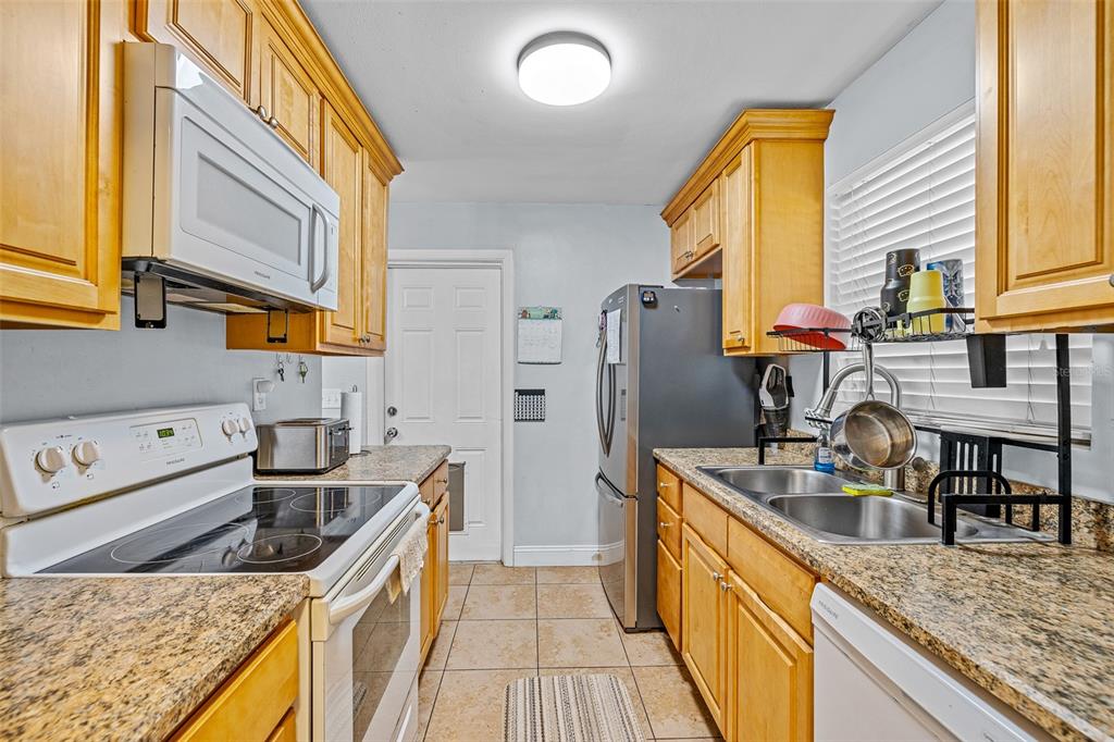 A galley kitchen features light wood cabinets, granite countertops, stainless steel appliances, and tile flooring — 2821 OAK LEA DRIVE, SOUTH DAYTONA, FL