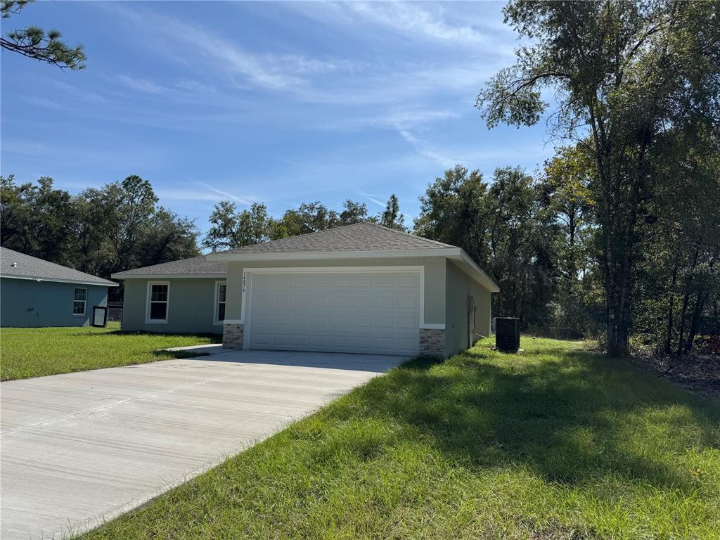 A single-story house with a two-car garage, light green siding, and a concrete driveway — 17603 SW 112TH LANE, DUNNELLON, FL