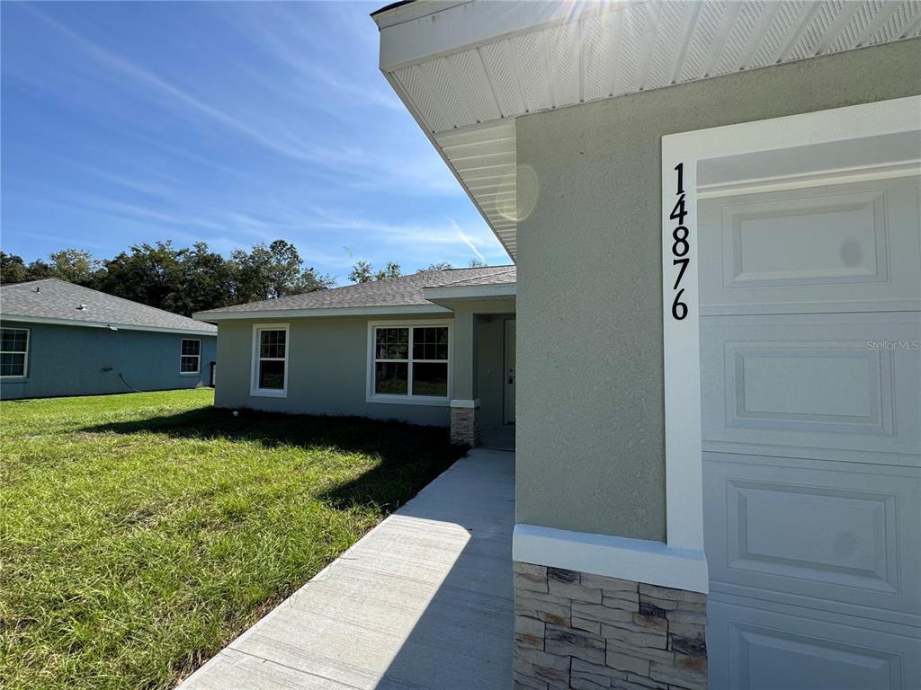 The exterior of a light green house features a concrete walkway and a garage door — 17603 SW 112TH LANE, DUNNELLON, FL
