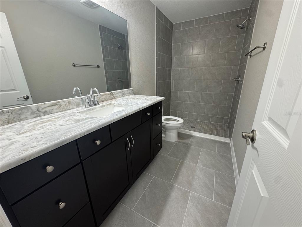 A bathroom features a dark vanity with a marble countertop, gray tiled flooring, and a shower — 17603 SW 112TH LANE, DUNNELLON, FL