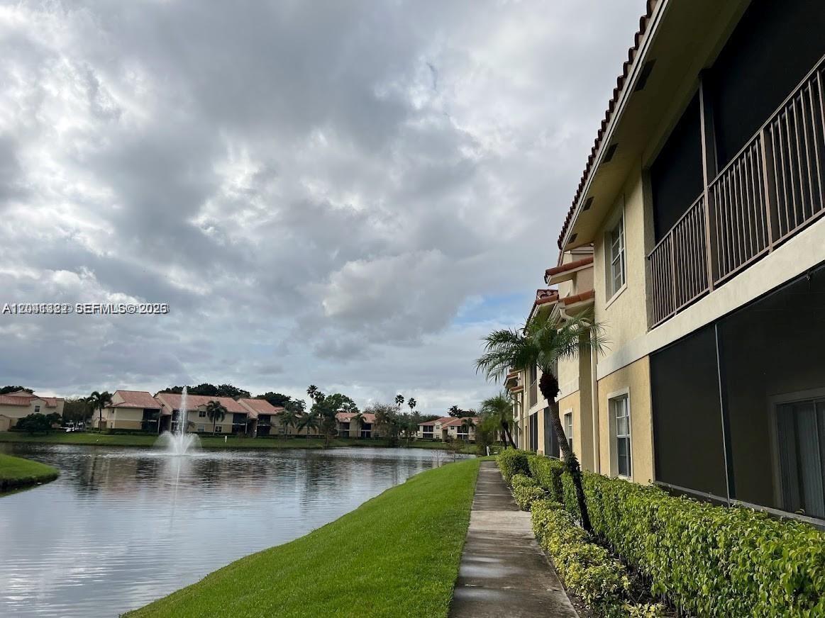 A concrete walkway runs alongside a residential building and a lake with a fountain — 1227 SW 46th Ave # 304, Pompano Beach FL 33069, POMPANO BEACH, FL