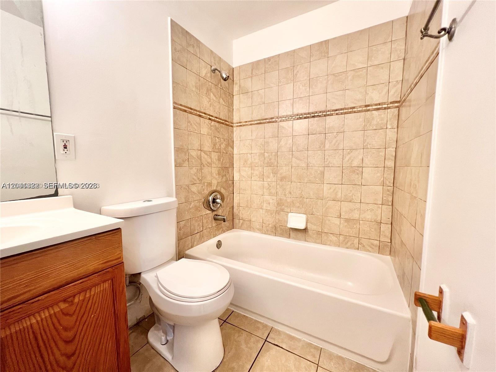 A bathroom features a wooden vanity, a white toilet, and a tiled bathtub shower surround — 1227 SW 46th Ave # 304, Pompano Beach FL 33069, POMPANO BEACH, FL
