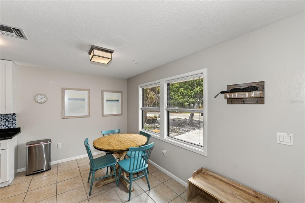 A dining area features a round wooden table, teal chairs, tile flooring, and a window view — 2475 ALAMEDA AVENUE UNIT B, SARASOTA, FL