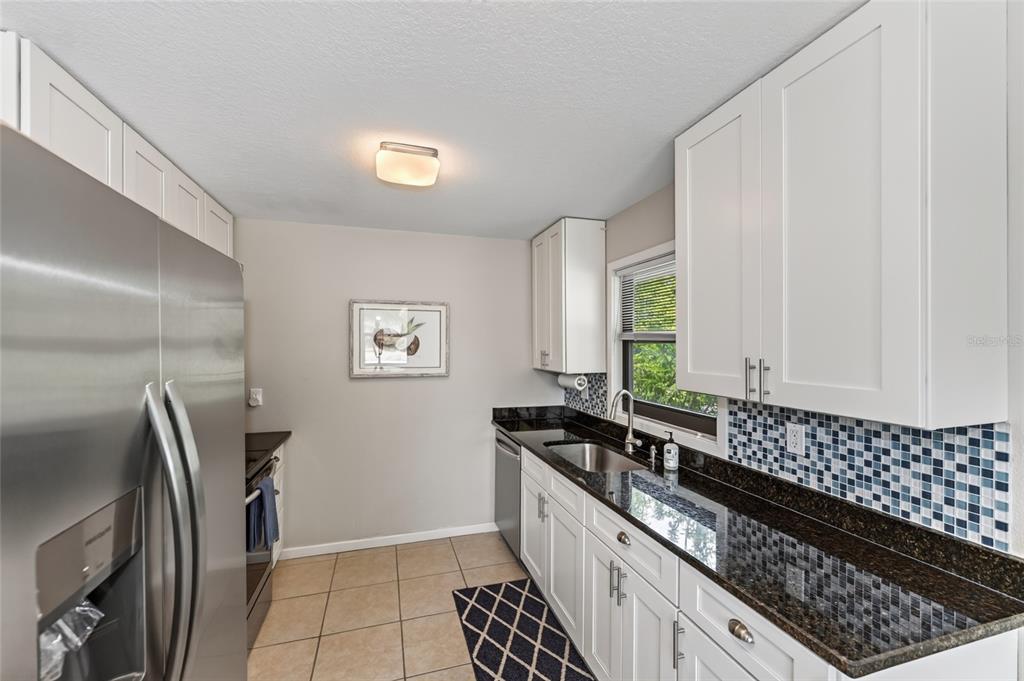 A kitchen features white cabinets, dark granite countertops, stainless steel appliances, and a blue-tiled backsplash — 2475 ALAMEDA AVENUE UNIT B, SARASOTA, FL