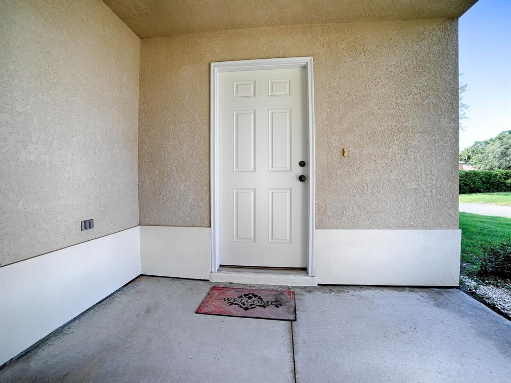 A white front door with a welcome mat is centered on a covered concrete porch — 12319 NE 52ND LOOP, OXFORD, FL
