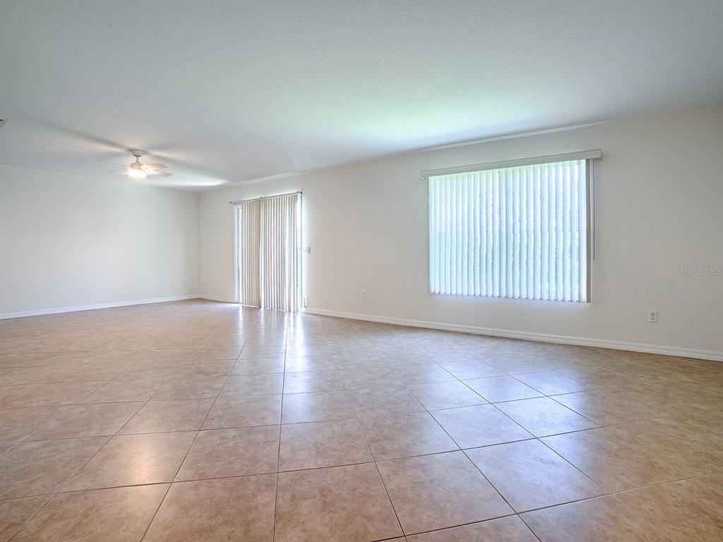 An empty room with beige tile flooring, white walls, a ceiling fan, and vertical blinds — 12319 NE 52ND LOOP, OXFORD, FL
