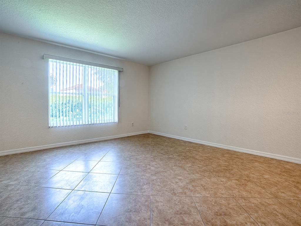 An empty room features beige tile flooring, white walls, and a window with vertical blinds — 12319 NE 52ND LOOP, OXFORD, FL