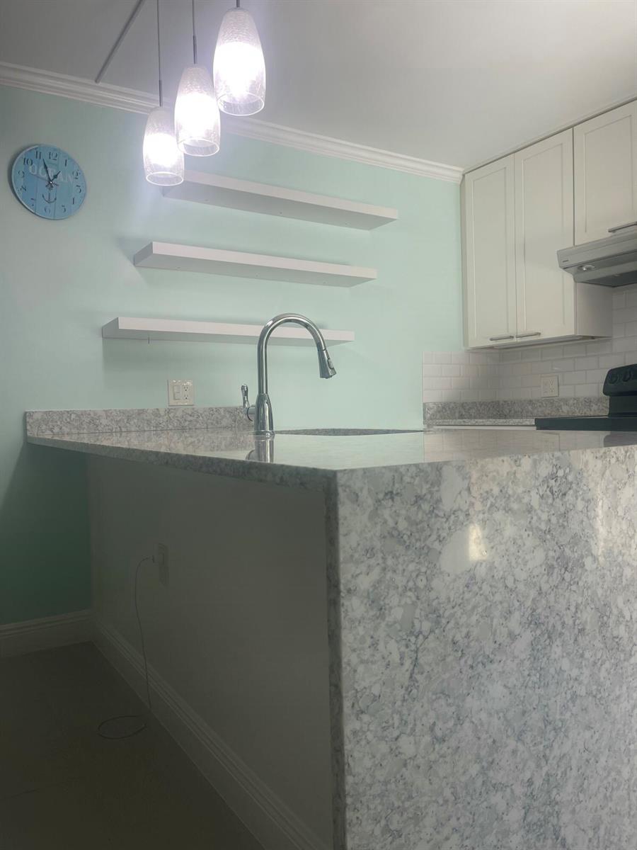 A kitchen features a granite countertop island, white floating shelves, and light green walls — 1612 16th Court, Jupiter FL 33477, JUPITER, FL