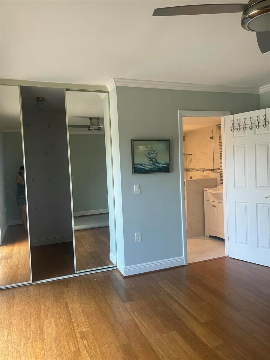 A bedroom features hardwood floors, mirrored closet doors, a framed painting, and an attached bathroom — 1612 16th Court, Jupiter FL 33477, JUPITER, FL