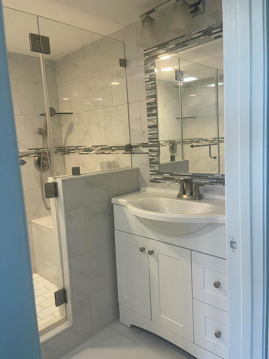 A bathroom features a white vanity, a glass-enclosed shower with marble-look tiles, and a mirror — 1612 16th Court, Jupiter FL 33477, JUPITER, FL