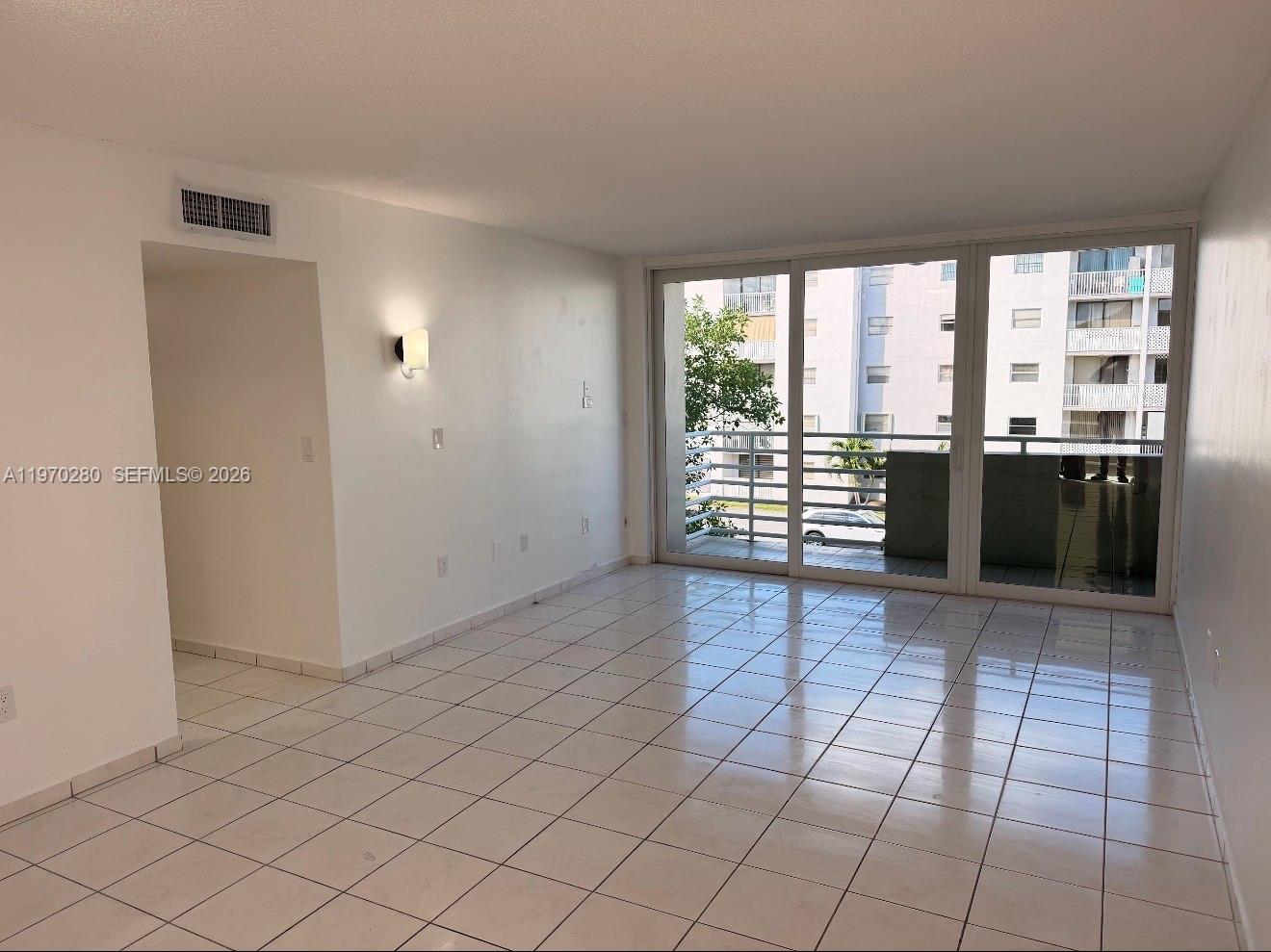 An empty living room features white tile flooring, a wall sconce, and a sliding glass door — 8050 NW 8th St # 1307, Miami FL 33126, MIAMI, FL