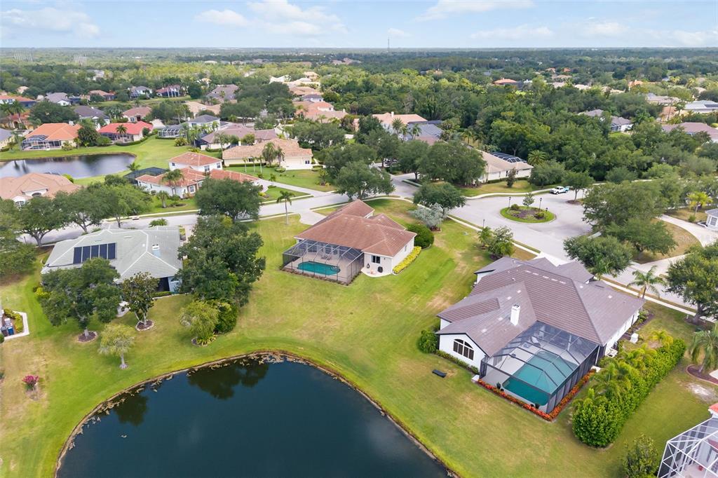 An aerial view shows several houses with screened-in pools situated around a small lake — 7505 COVENTRY COURT, BRADENTON, FL