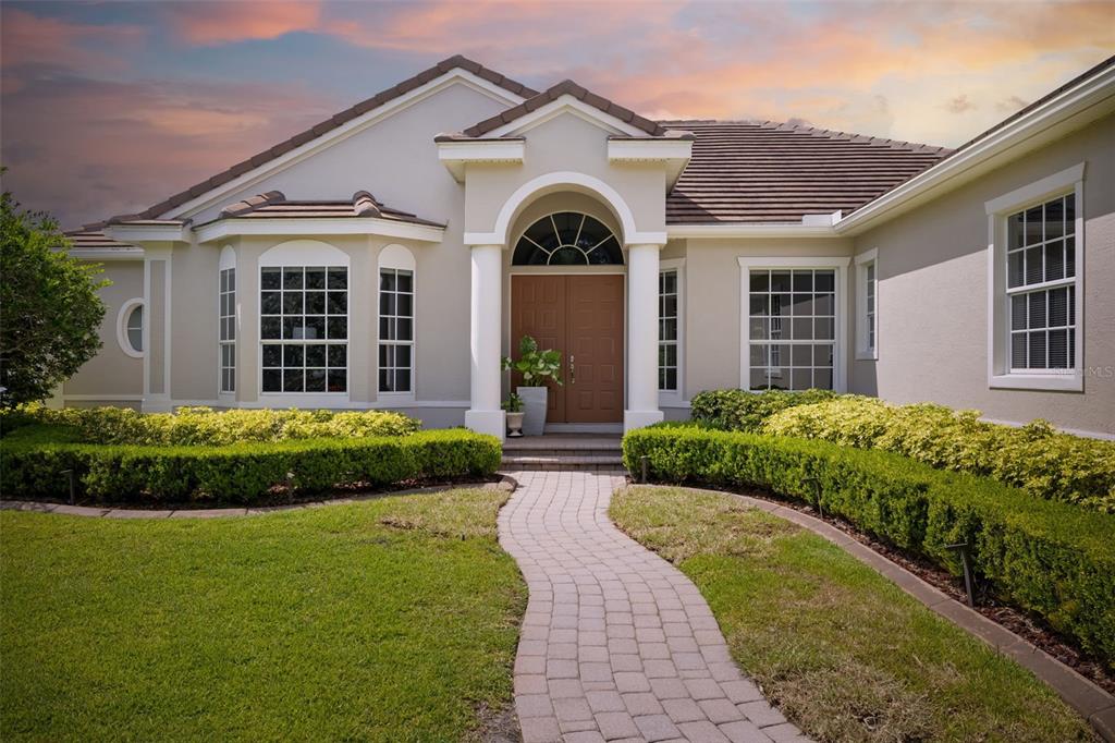 A single-story house with a beige exterior, arched entryway, and a brick walkway — 7505 COVENTRY COURT, BRADENTON, FL