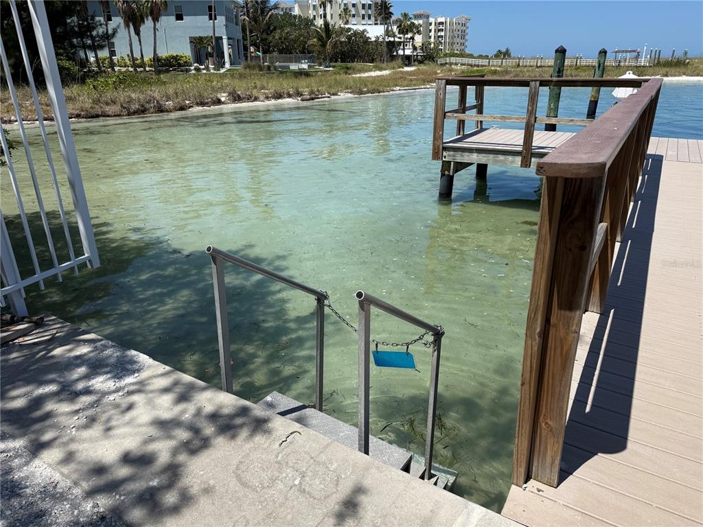 A concrete staircase leads into shallow water next to a wooden dock and railing — 1100 PINELLAS BAYWAY S UNIT G2, TIERRA VERDE, FL