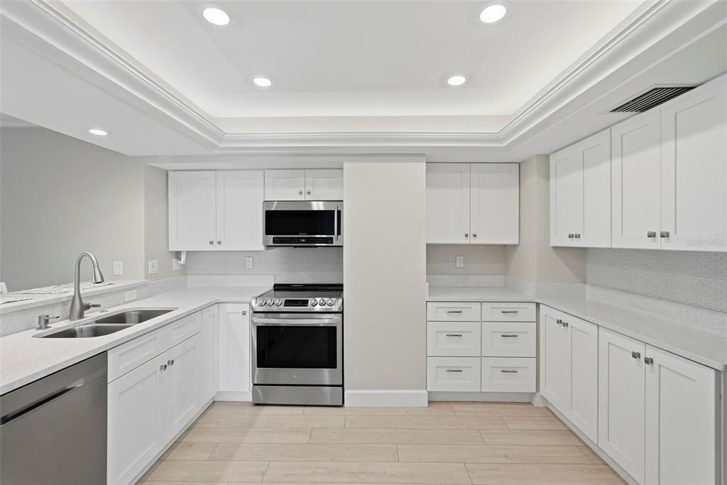 A modern kitchen features white cabinets, stainless steel appliances, quartz countertops, and light wood flooring — 1100 PINELLAS BAYWAY S UNIT G2, TIERRA VERDE, FL
