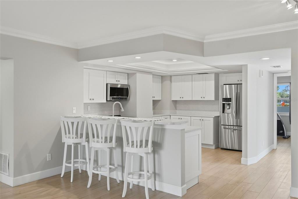 A modern kitchen features white cabinetry, stainless steel appliances, and a breakfast bar with stools — 1100 PINELLAS BAYWAY S UNIT G2, TIERRA VERDE, FL