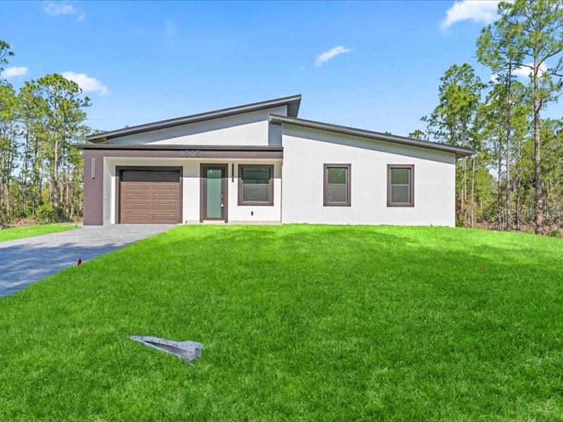 A modern, single-story house with a white exterior, dark trim, and a front-facing garage — 1305 MCARTHUR AVENUE, LEHIGH ACRES, FL