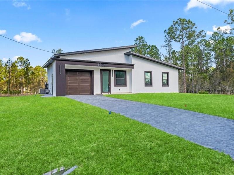 A modern single-story house with a white exterior, dark trim, and a paved driveway — 1305 MCARTHUR AVENUE, LEHIGH ACRES, FL