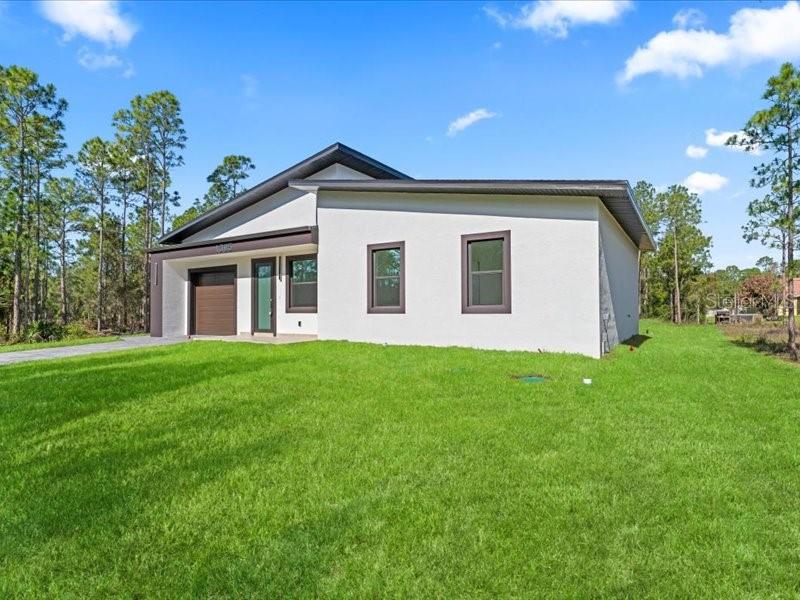 A modern, single-story white house with a brown garage door sits on a grassy lot — 1305 MCARTHUR AVENUE, LEHIGH ACRES, FL