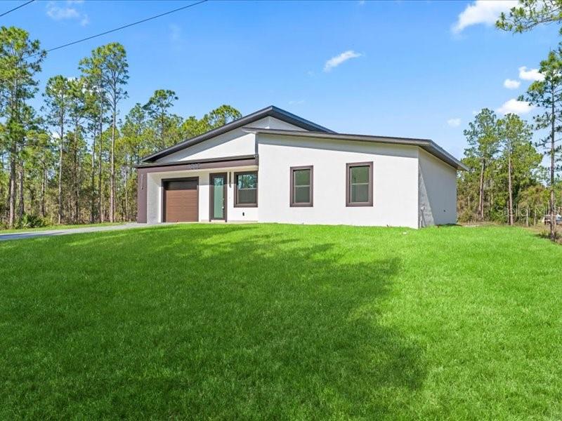 A modern, single-story white house with a dark roof and garage sits on a lawn — 1305 MCARTHUR AVENUE, LEHIGH ACRES, FL