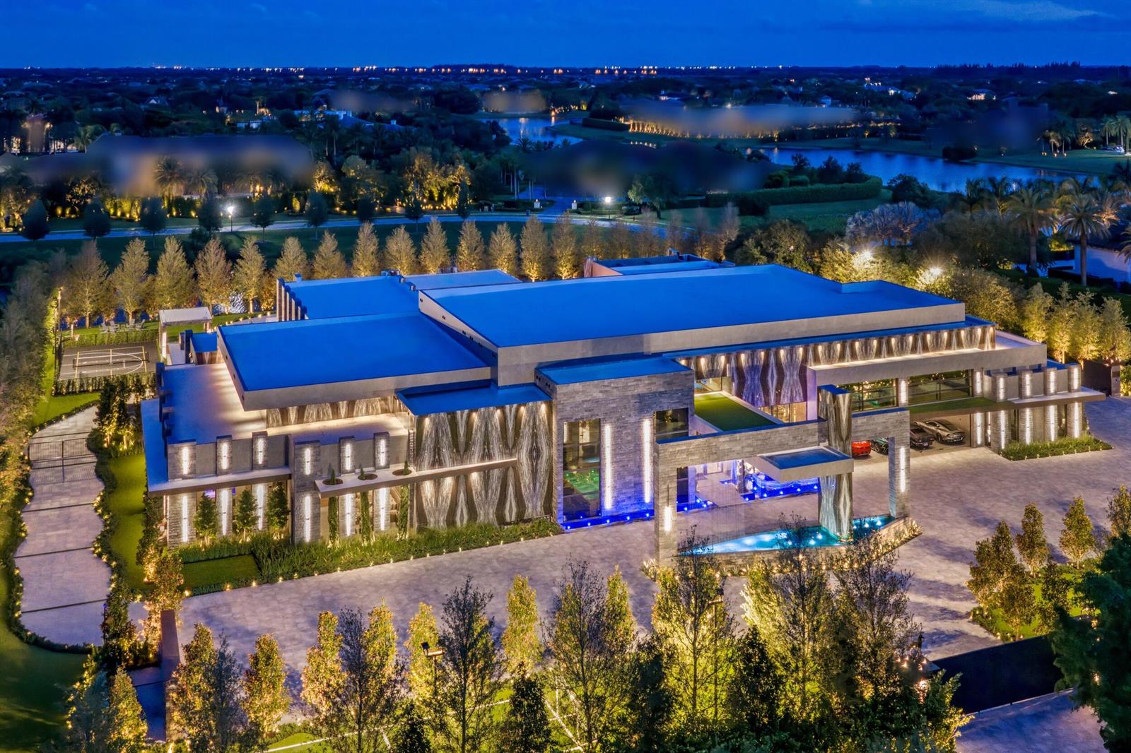 An aerial view of a modern luxury mansion at night with a large paved driveway — 16121 Quiet Vista Circle, Delray Beach FL 33446, DELRAY BEACH, FL