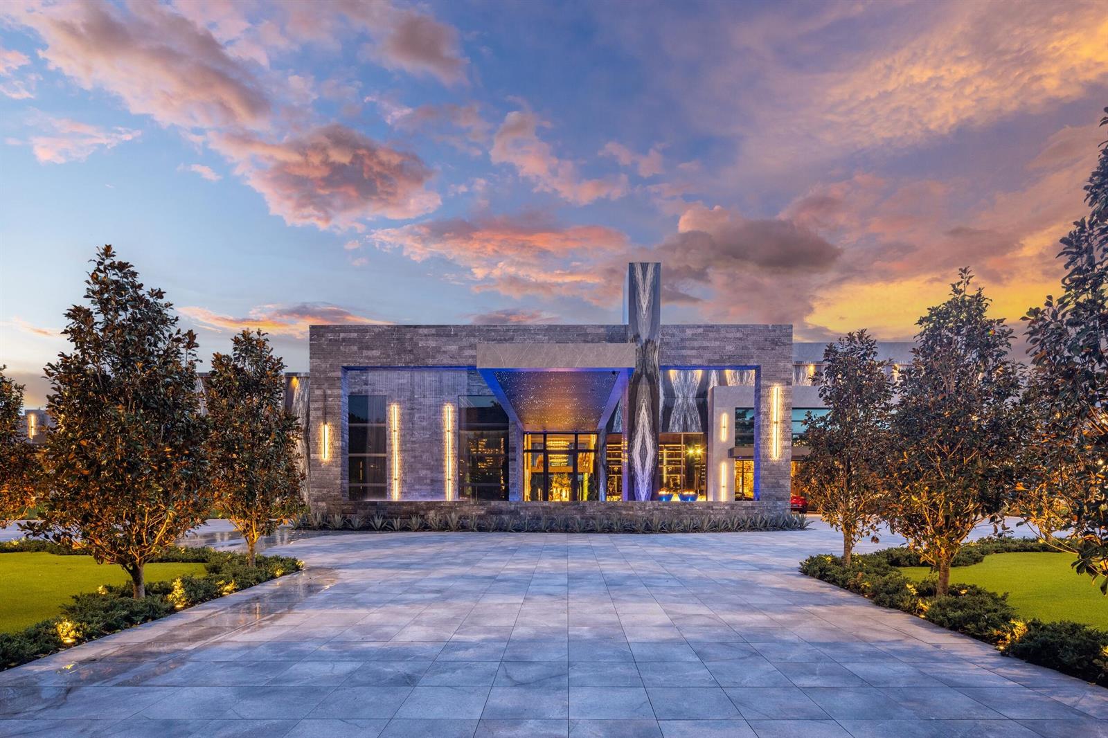 A modern stone mansion exterior features a grand entrance with blue lighting at dusk — 16121 Quiet Vista Circle, Delray Beach FL 33446, DELRAY BEACH, FL