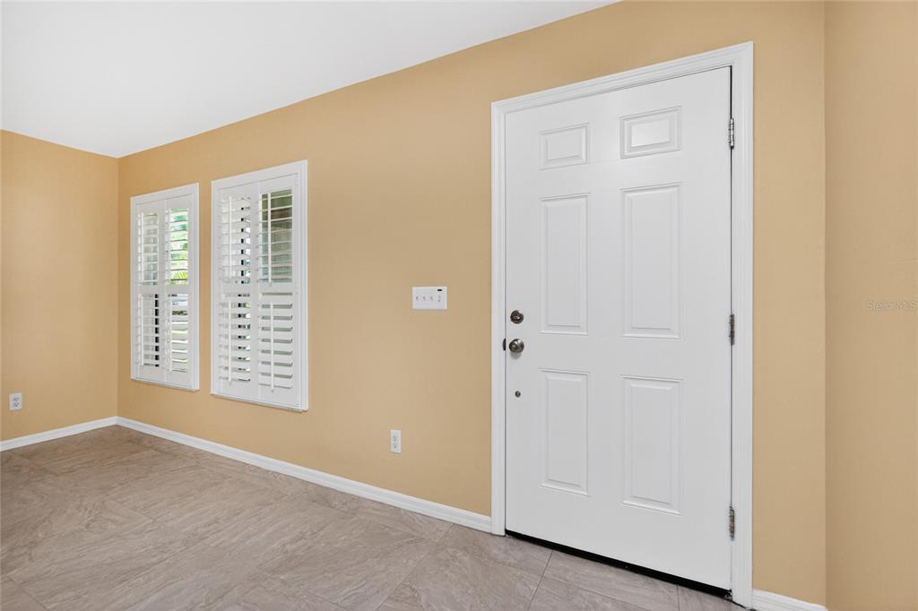 An entryway with tan walls, tile flooring, a white front door, and plantation shutters — 17200 NILE CT, PUNTA GORDA, FL