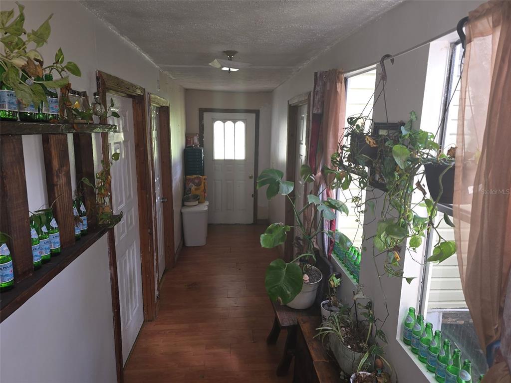 A narrow hallway with wood flooring, multiple doors, and numerous potted plants along the windows — 12510 ROBINHOOD ROAD, HUDSON, FL