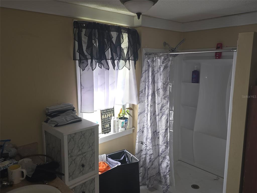 A bathroom features a white shower stall, a window with a valance, and a storage cabinet — 12510 ROBINHOOD ROAD, HUDSON, FL