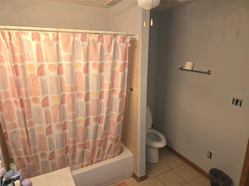 A bathroom features a shower with a patterned curtain, a toilet, and a towel rack — 12510 ROBINHOOD ROAD, HUDSON, FL