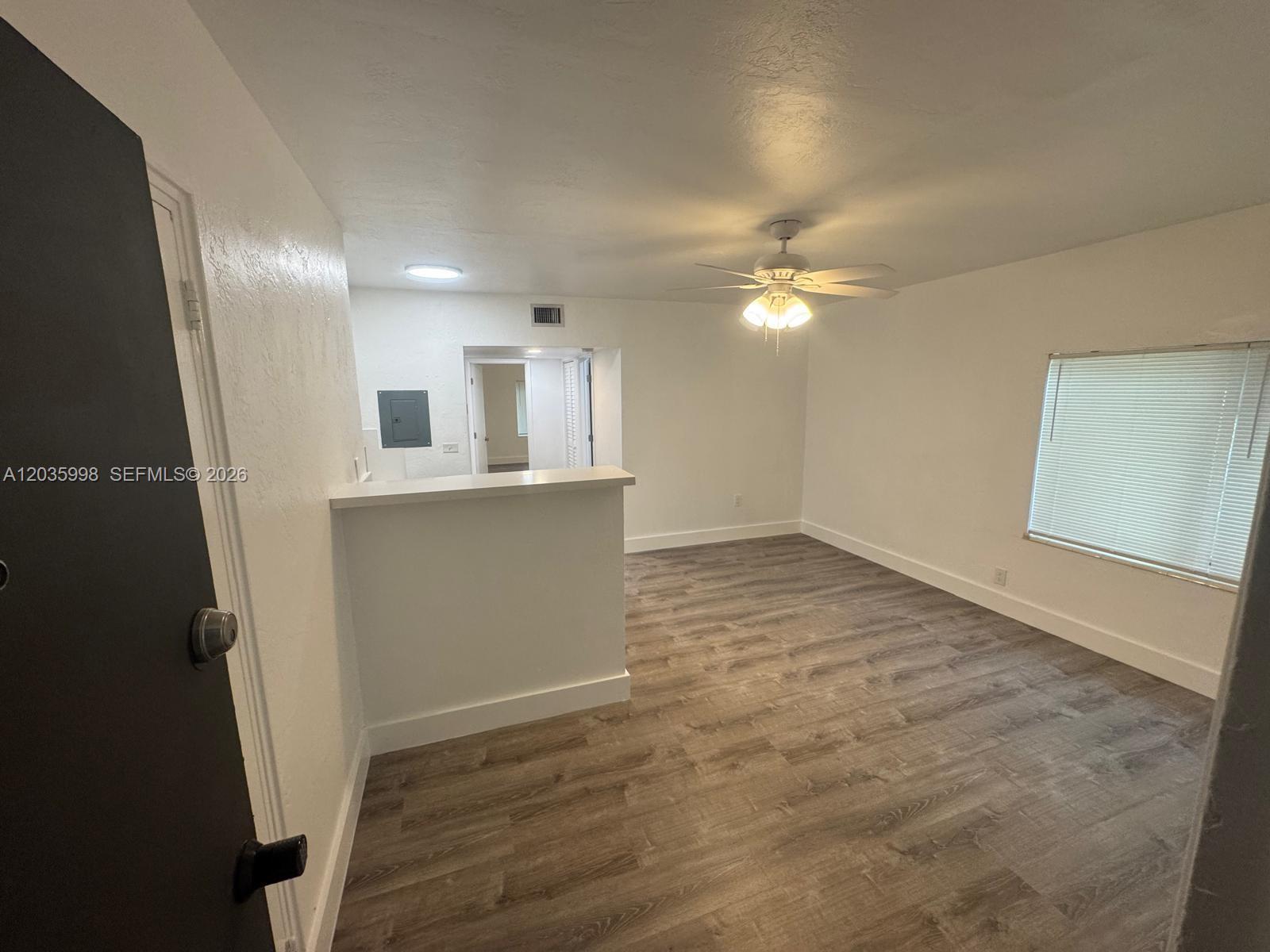 An empty room features wood-look flooring, a ceiling fan, and a partial partition wall — 350 SW 15th Rd # 9, Miami FL 33129, MIAMI, FL