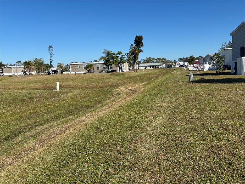 A grassy field slopes toward several manufactured homes under a clear blue sky — 7381 PETULA AVE, PORT CHARLOTTE, FL