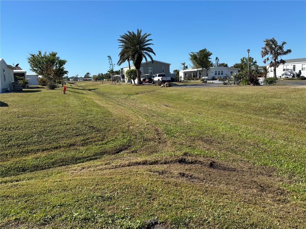 A grassy field with tire tracks leads toward several manufactured homes and palm trees — 7381 PETULA AVE, PORT CHARLOTTE, FL