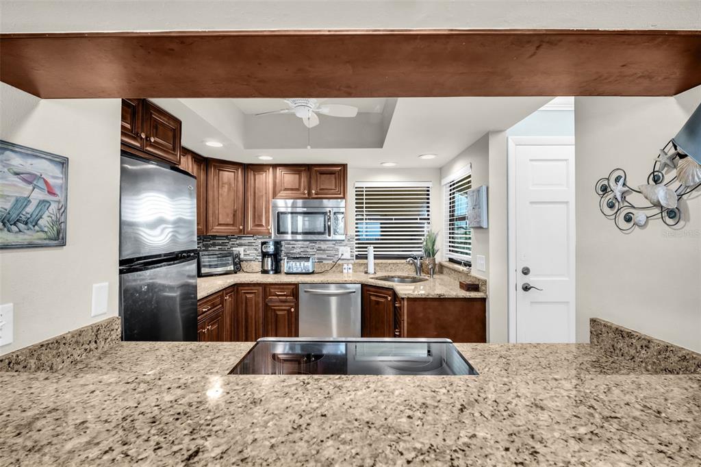 A kitchen with dark wood cabinets, granite countertops, and stainless steel appliances viewed from above — 3500 GULF BOULEVARD UNIT 407B, BELLEAIR BEACH, FL