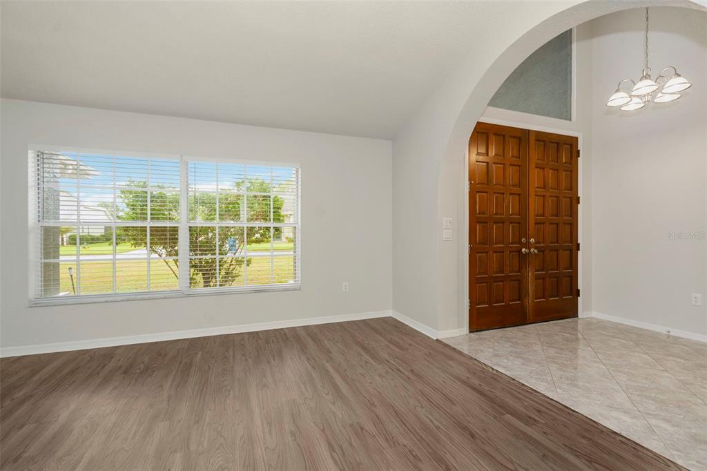 A room with wood-look flooring, a large window, and an arched entryway to a tiled foyer — 9396 SOUTHERN BELLE DRIVE, BROOKSVILLE, FL