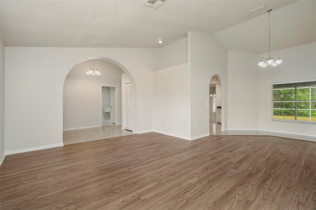 A bright, open-concept living area features wood-look flooring, arched entryways, and a vaulted ceiling — 9396 SOUTHERN BELLE DRIVE, BROOKSVILLE, FL