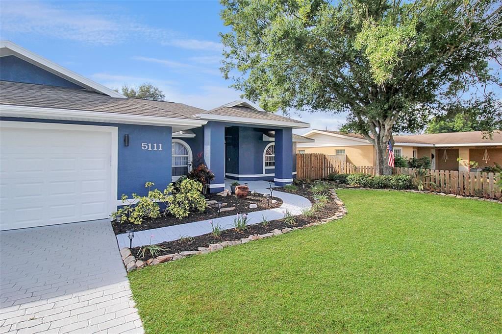 A blue house with a white garage door and a curved walkway through the yard — 5111 13TH AVENUE DRIVE W, BRADENTON, FL