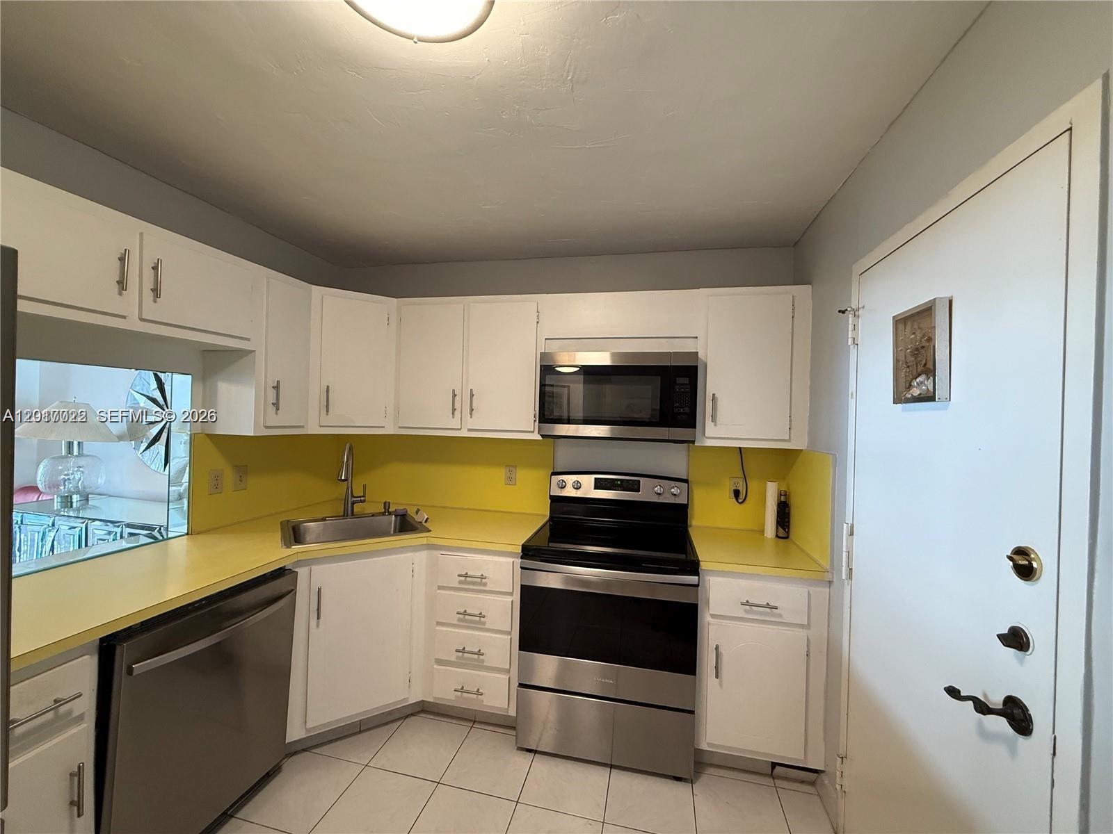 A kitchen features white cabinets, yellow countertops, stainless steel appliances, and light-colored floor tiles — 1865 S Ocean Dr # 15C, Hallandale Beach FL 33009, HALLANDALE BEACH, FL
