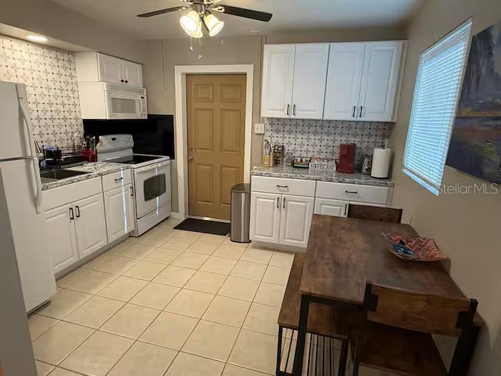 A kitchen features white cabinets, patterned tile backsplashes, tile flooring, and a wooden dining set — 525 SHOWALTER AVENUE, PUNTA GORDA, FL