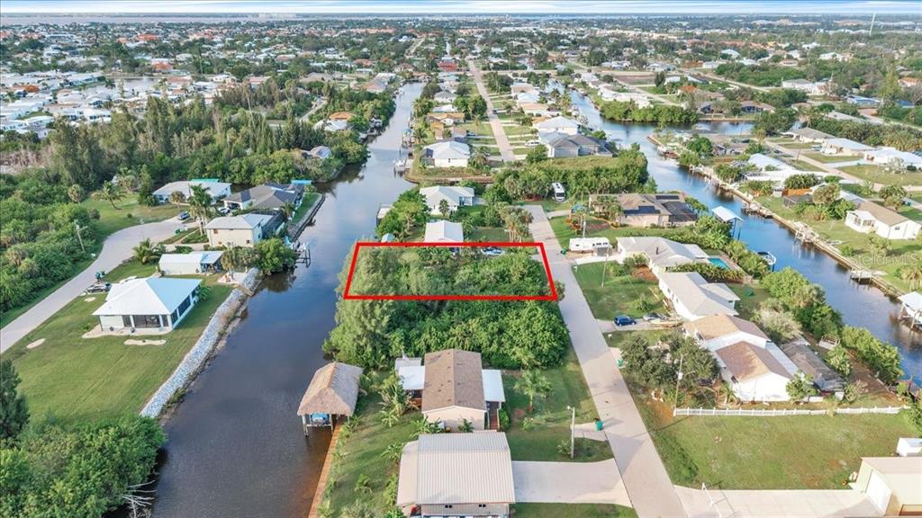 An aerial view shows a vacant, tree-covered lot outlined in red between a canal and road — 3623 MAGNOLIA WAY, PUNTA GORDA, FL