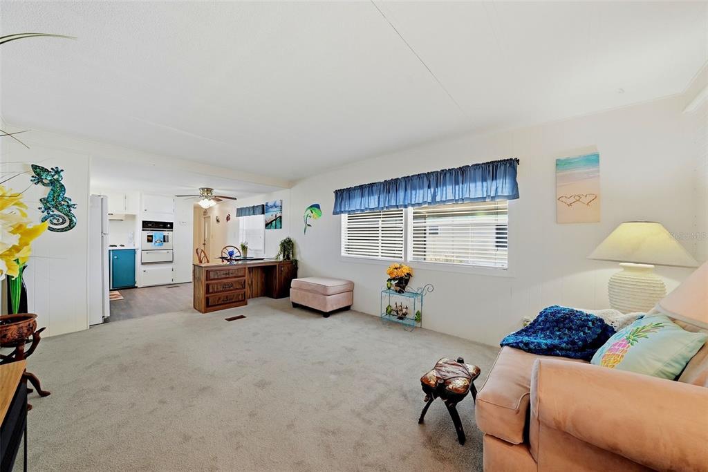 A living room with gray carpet, a wooden desk, and a view into the kitchen — 12116 HORSESHOE LANE, HUDSON, FL