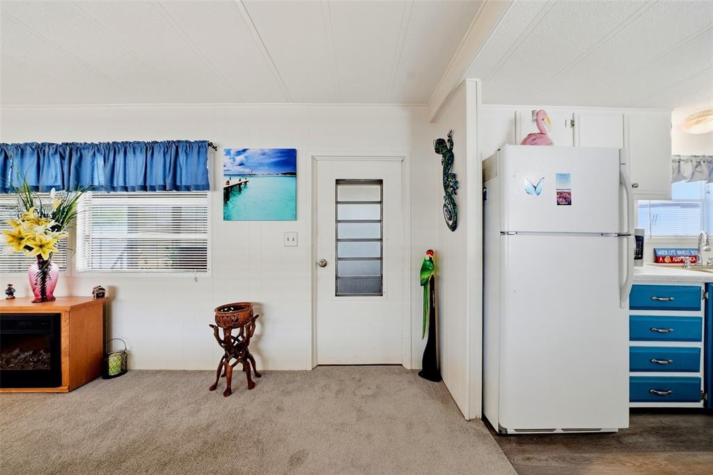 A room with carpeted flooring, a white door, a white refrigerator, and blue cabinets — 12116 HORSESHOE LANE, HUDSON, FL